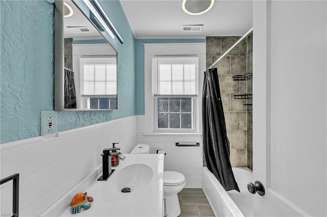 full bathroom featuring visible vents, toilet, a wainscoted wall, and shower / tub combo