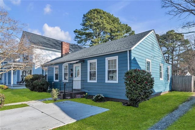 view of front of home with a shingled roof, a front yard, fence, and a chimney