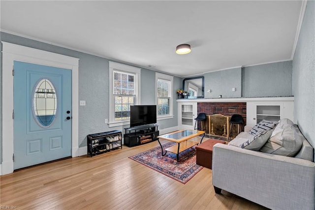 living room with wood finished floors, baseboards, ornamental molding, a brick fireplace, and a textured wall