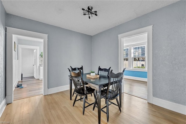 dining space featuring light wood-style flooring, a textured ceiling, baseboards, and a textured wall