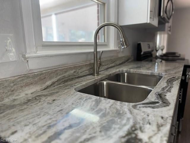 interior details with a sink, light stone counters, and white cabinets