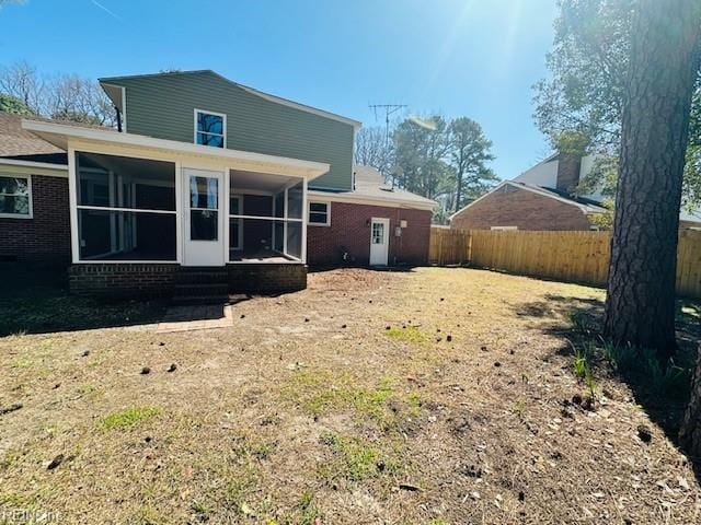 rear view of house featuring brick siding, fence, and a sunroom