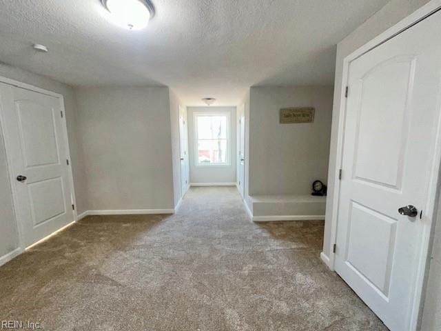 corridor featuring baseboards, carpet floors, and a textured ceiling