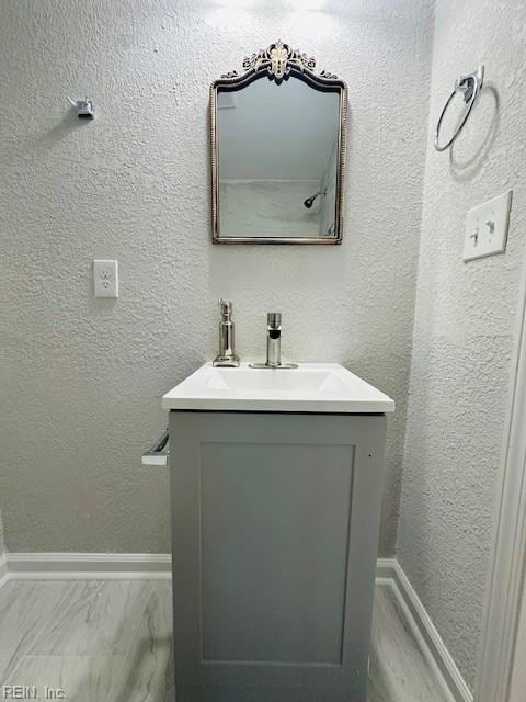 bathroom featuring baseboards, marble finish floor, vanity, and a textured wall