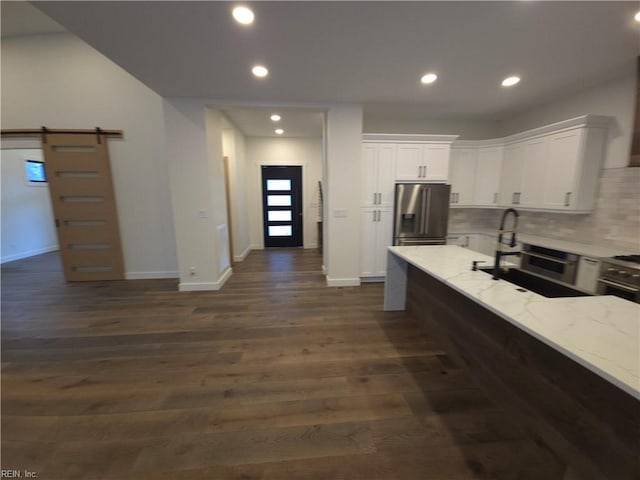 kitchen featuring dark wood-style floors, a barn door, stainless steel fridge, white cabinets, and light stone countertops