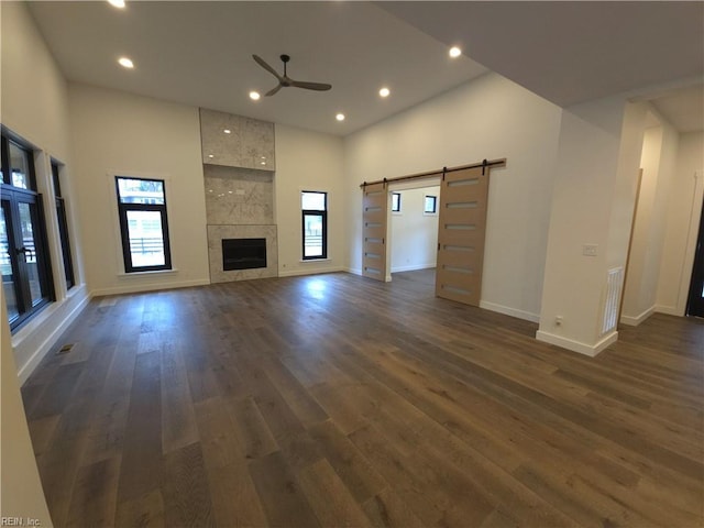 unfurnished living room featuring a barn door, plenty of natural light, and dark wood-style floors