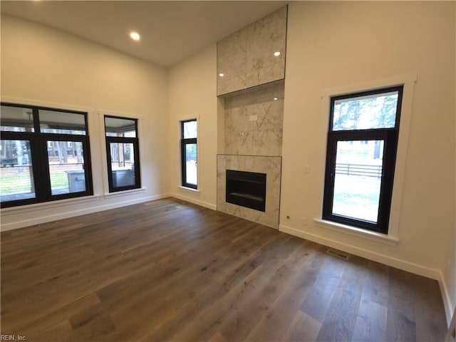 unfurnished living room with visible vents, dark wood finished floors, a high ceiling, baseboards, and a tile fireplace