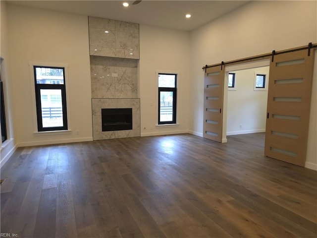 unfurnished living room featuring dark wood-style floors, recessed lighting, a barn door, a fireplace, and baseboards