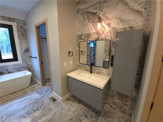 bathroom with tile walls, a freestanding bath, marble finish floor, and vanity