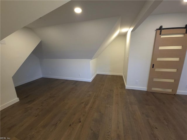 additional living space with a barn door, baseboards, lofted ceiling, and dark wood-style floors