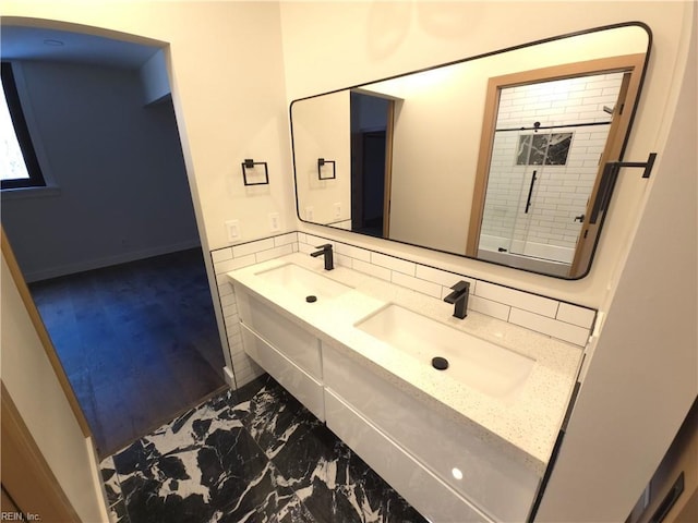 bathroom featuring a sink, a shower, marble finish floor, and double vanity