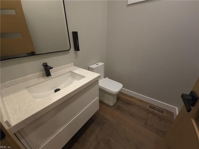 half bathroom featuring vanity, wood finished floors, visible vents, baseboards, and toilet