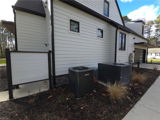 view of side of home featuring central air condition unit and roof with shingles