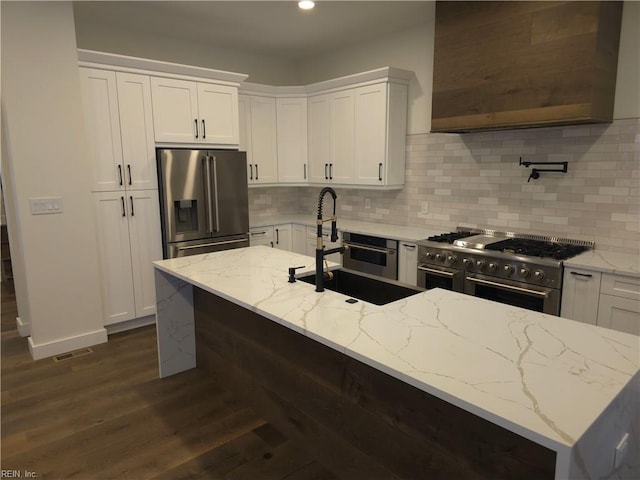 kitchen featuring dark wood-style floors, a sink, stainless steel appliances, white cabinets, and wall chimney exhaust hood