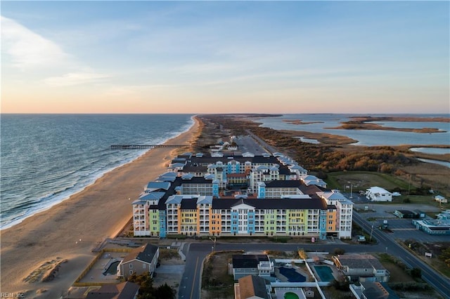 aerial view at dusk featuring a water view and a view of the beach