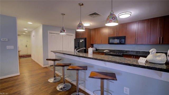 kitchen featuring visible vents, pendant lighting, a kitchen breakfast bar, wood finished floors, and black appliances