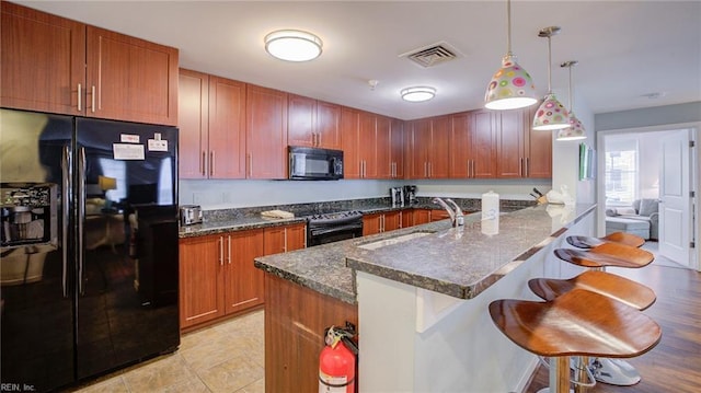 kitchen with a breakfast bar area, visible vents, a sink, black appliances, and brown cabinets