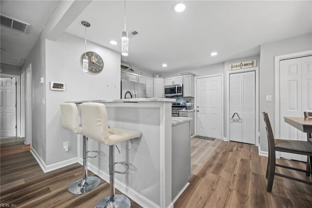 kitchen with decorative backsplash, appliances with stainless steel finishes, a breakfast bar area, and wood finished floors