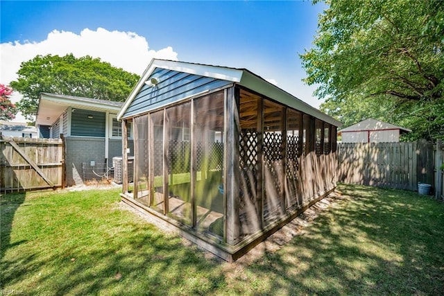 view of outbuilding with central AC unit, a fenced backyard, and a sunroom