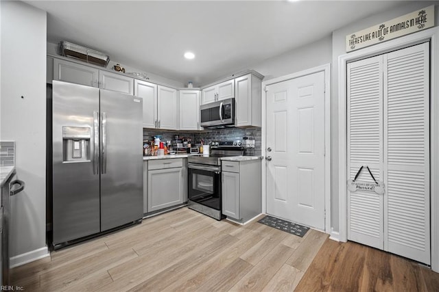 kitchen with light wood-type flooring, backsplash, appliances with stainless steel finishes, and gray cabinets