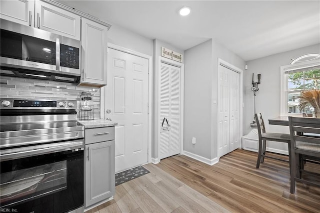 kitchen featuring tasteful backsplash, baseboards, light wood-type flooring, light stone counters, and stainless steel appliances