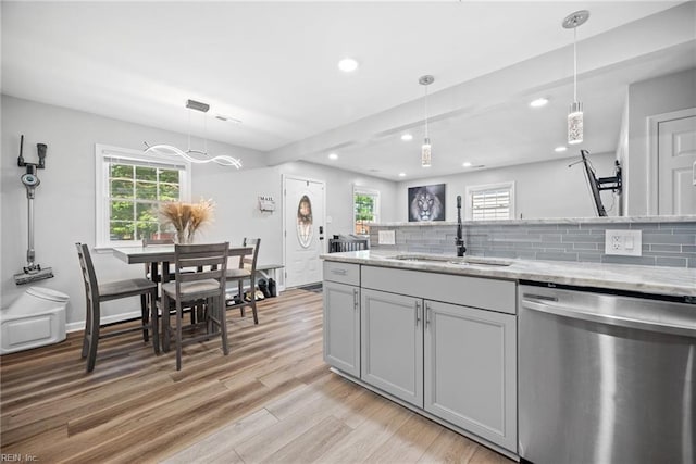 kitchen with stainless steel dishwasher, light wood-style floors, tasteful backsplash, and a sink