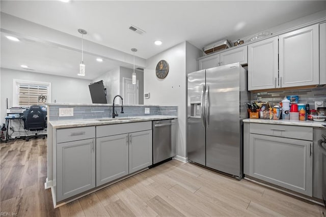 kitchen with decorative light fixtures, light wood-style flooring, appliances with stainless steel finishes, a peninsula, and a sink