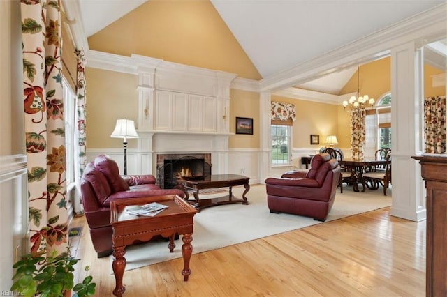 living area featuring wood finished floors, high vaulted ceiling, an inviting chandelier, a fireplace, and wainscoting