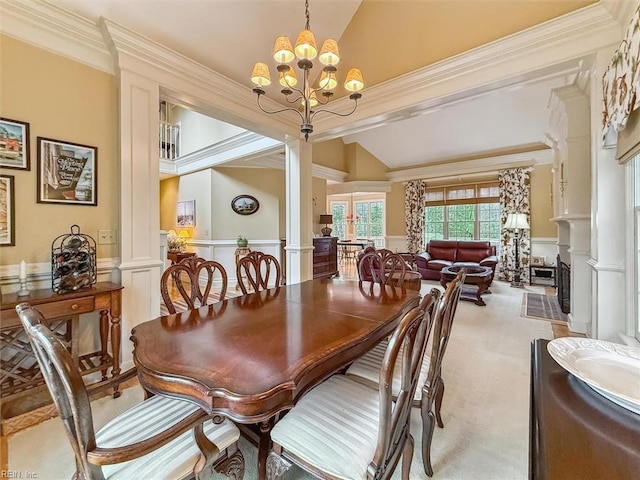 carpeted dining room featuring a wainscoted wall, lofted ceiling, decorative columns, crown molding, and a chandelier