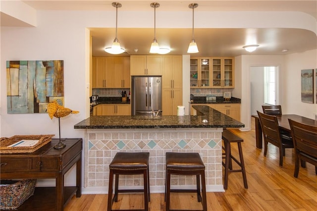 kitchen featuring tasteful backsplash, freestanding refrigerator, light wood-style floors, a peninsula, and a breakfast bar area