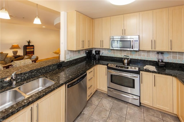 kitchen featuring backsplash, light brown cabinetry, dark stone counters, appliances with stainless steel finishes, and a sink