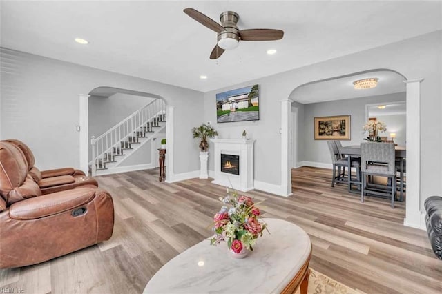 living room with stairs, light wood-style floors, arched walkways, and a warm lit fireplace