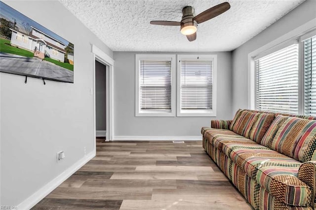 living room featuring a ceiling fan, wood finished floors, baseboards, and a textured ceiling