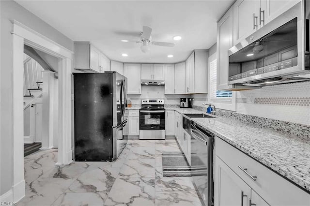 kitchen with light stone counters, recessed lighting, a sink, stainless steel appliances, and under cabinet range hood