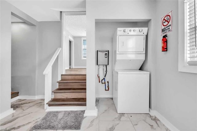 washroom featuring baseboards, stacked washer and dryer, laundry area, marble finish floor, and a textured ceiling