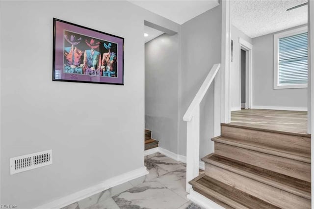 stairs featuring a textured ceiling, visible vents, marble finish floor, and baseboards