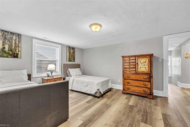 bedroom with light wood finished floors, visible vents, and baseboards