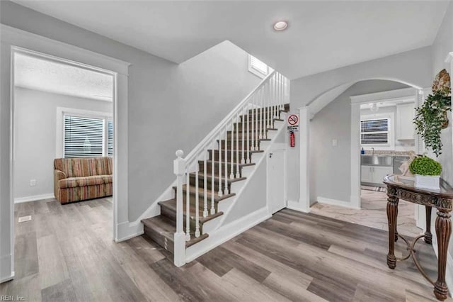 staircase featuring arched walkways, baseboards, and wood finished floors