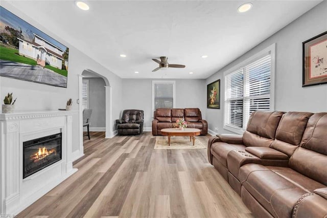 living area with a glass covered fireplace, recessed lighting, arched walkways, and light wood finished floors