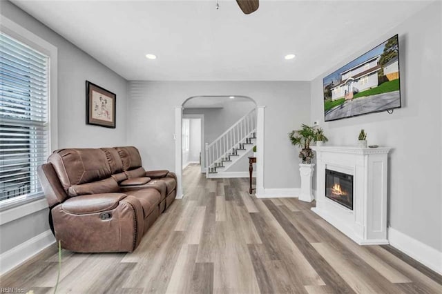 living area with arched walkways, stairway, baseboards, and wood finished floors