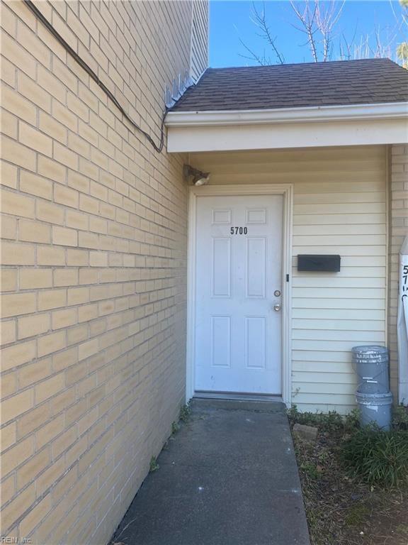 view of exterior entry with a shingled roof and brick siding