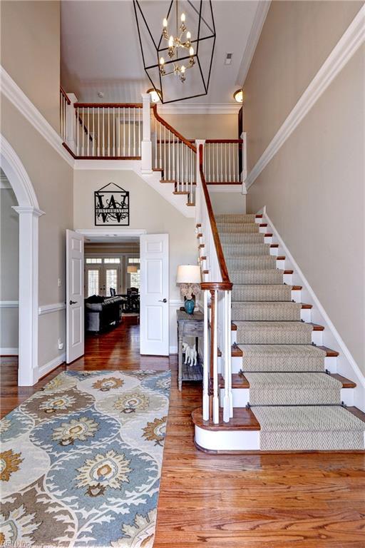 stairs with wood finished floors, baseboards, arched walkways, a towering ceiling, and crown molding