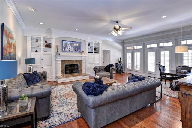 living area with a premium fireplace, ornamental molding, a ceiling fan, and wood finished floors