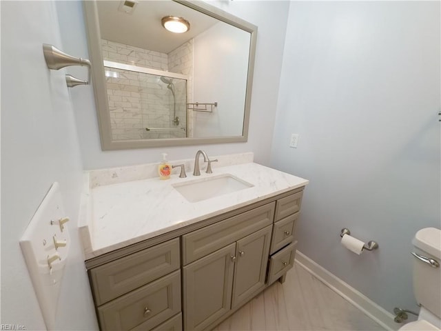 full bathroom featuring baseboards, toilet, vanity, and a tile shower