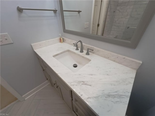 bathroom with tiled shower, vanity, and baseboards