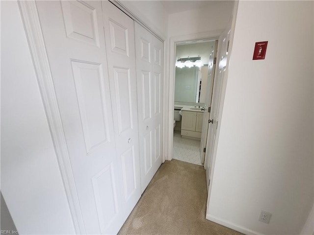 hallway with light colored carpet, baseboards, and a sink