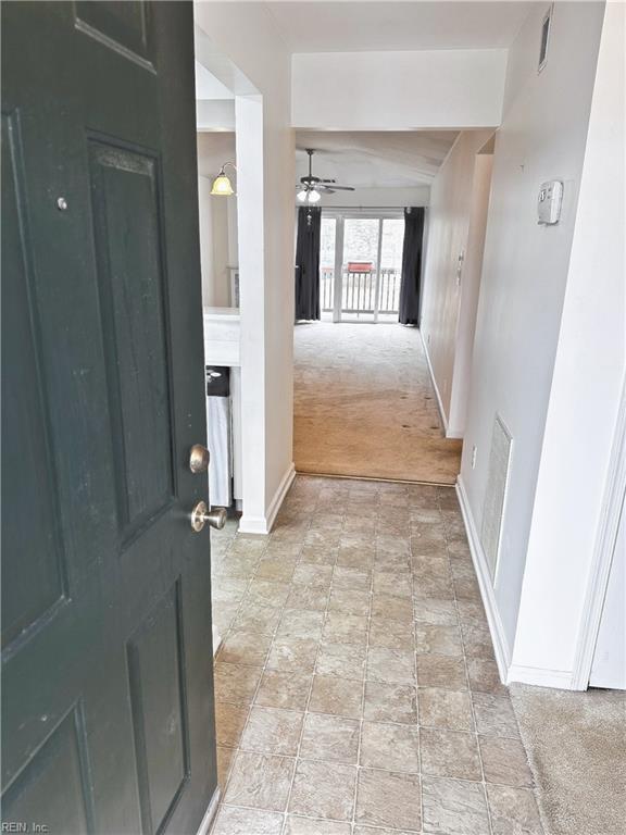 hallway with visible vents, baseboards, and light colored carpet