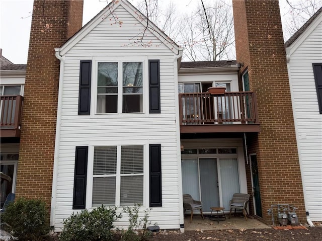 back of property featuring brick siding, a balcony, and a chimney