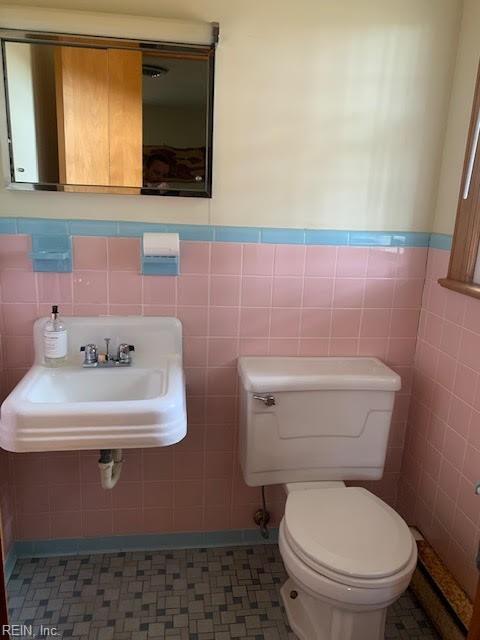 bathroom with tile walls, toilet, a wainscoted wall, and a sink