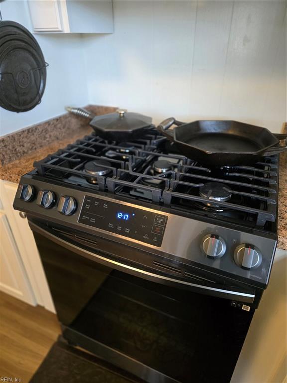 interior details with wood finished floors, stainless steel gas stove, and stone counters